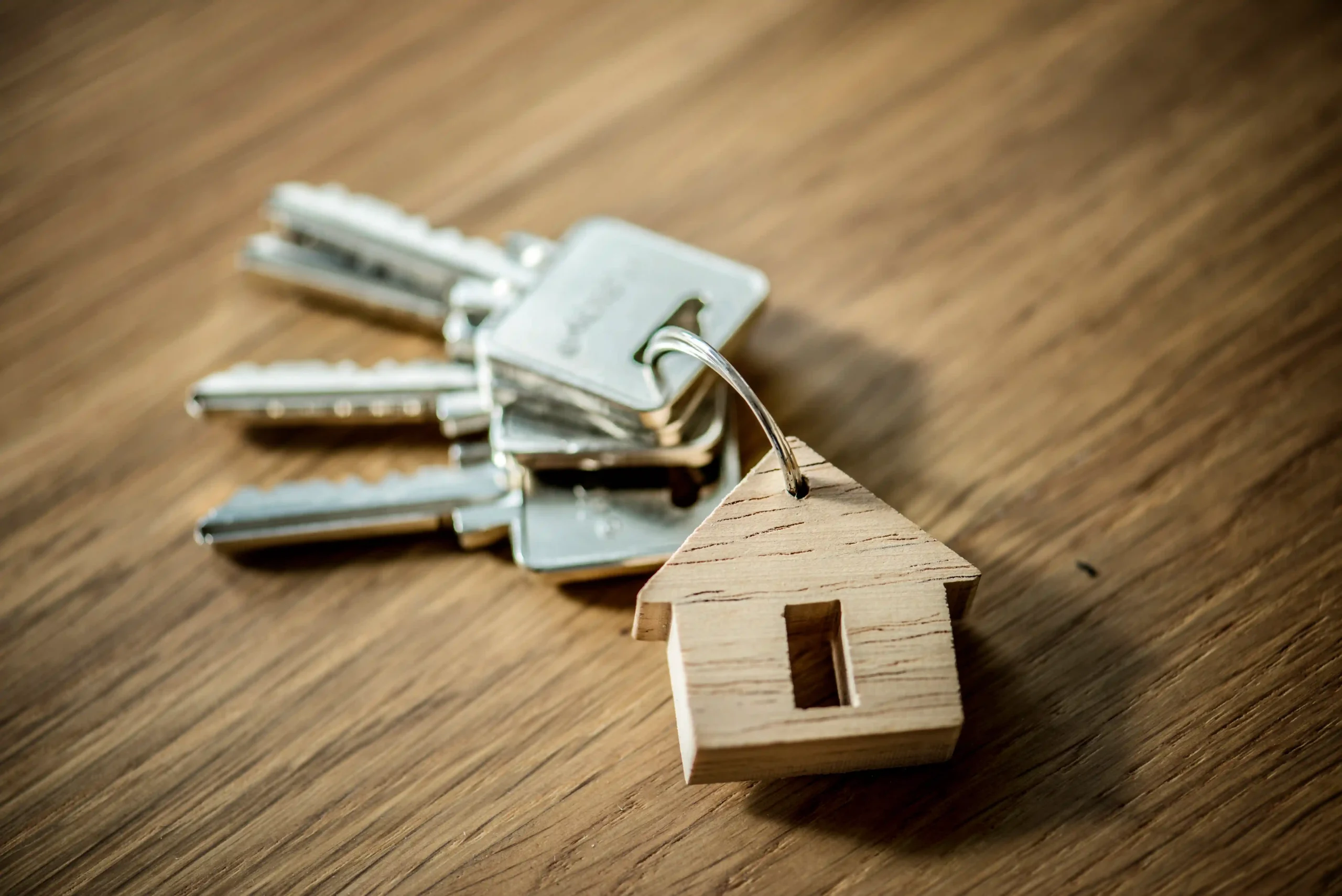Set of property keys with a wooden house-shaped keyring on a table.