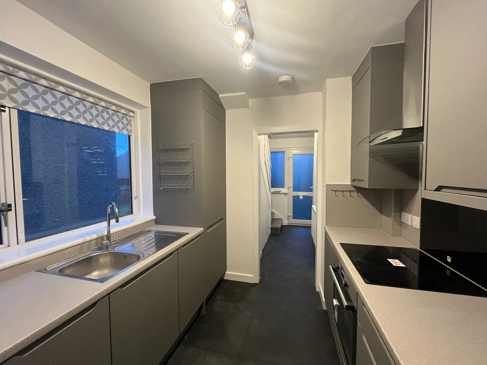 Refurbished galley kitchen with pale cabinets, dark worktops and a window above the sink.