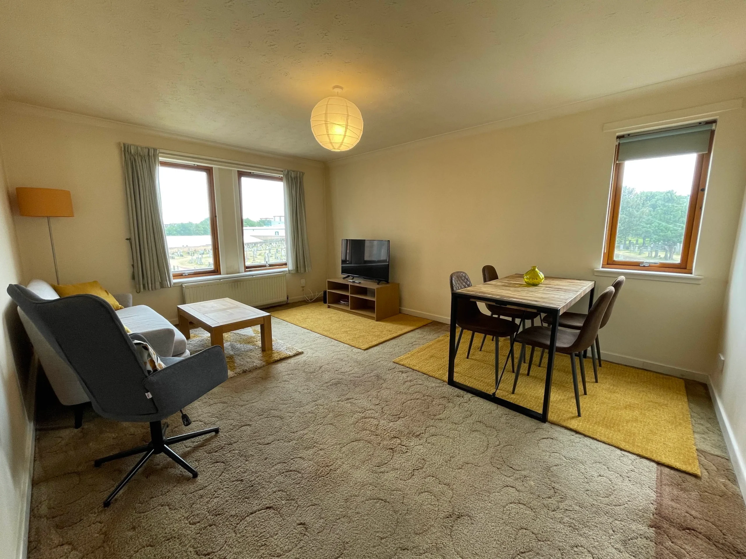 Living and dining room before renovation, with a grey sofa, large rug, coffee table and two windows.